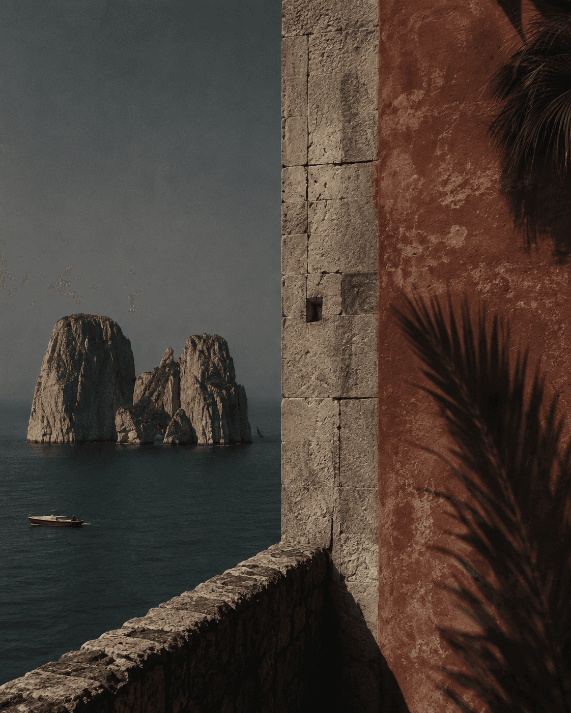 Felsformationen im Meer vor einer verwitterten mediterranen Mauer mit Palmwedel.